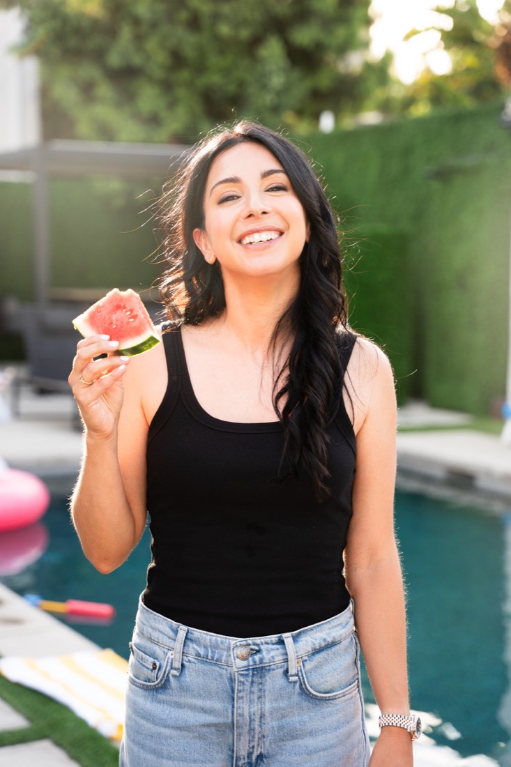 A woman holding a slice of watermelon by the pool